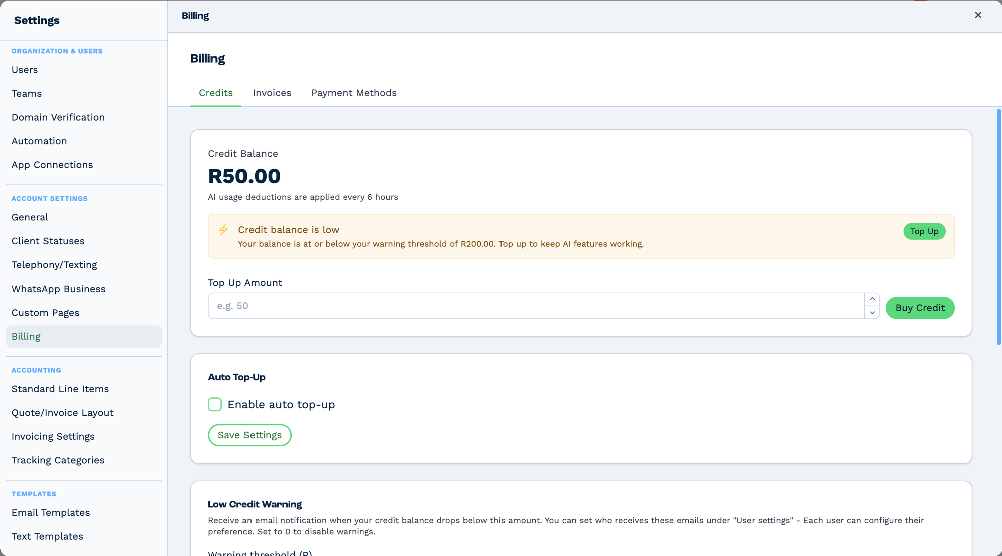 The Credits tab of the Billing screen in BaseCloud Settings, alongside Invoices and Payment Methods tabs. A Credit Balance is shown as a large figure, with a line beneath reading "AI usage deductions are applied every 6 hours". An amber notice reads "Credit balance is low — your balance is at or below your warning threshold. Top up to keep AI features working", with a Top Up button. Below are a Top Up Amount field with a Buy Credit button, an Auto Top-Up section with an unchecked "Enable auto top-up" box and a Save Settings button, and a Low Credit Warning section explaining that an email is sent when the balance drops below a threshold, that recipients are configured per user, and that setting it to zero disables warnings
